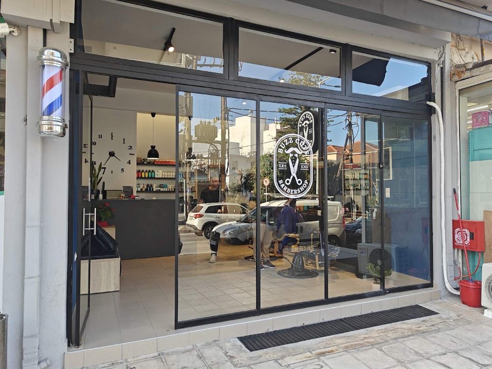 Η είσοδος του Buzz Cuts Barbershop στην Ηγουμένου Γαβριήλ, με τον στύλο του κουρείου και το logo στο τζάμι